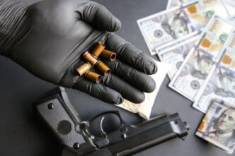 Hand in black glove holding bullet casings over gun and money