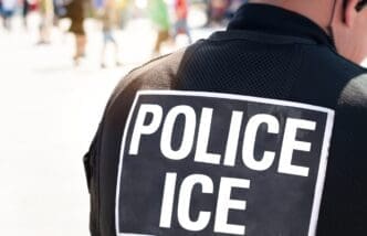 The back of a police officer's black vest with a large white sign that reads "POLICE ICE"