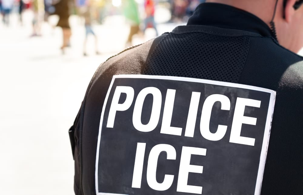 The back of a police officer's black vest with a large white sign that reads "POLICE ICE"