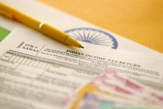 A yellow pen rests on an Indian Income Tax Return form with Indian currency in the foreground