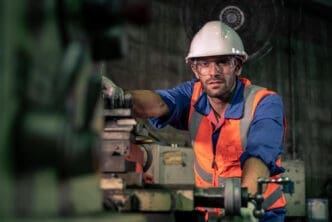 A male engineer in a hard hat and safety gear works on machinery in a factory