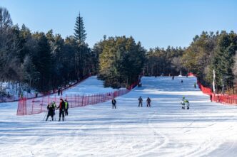 Skiers and snowboarders are spread across a snowy ski slope on a clear, sunny day