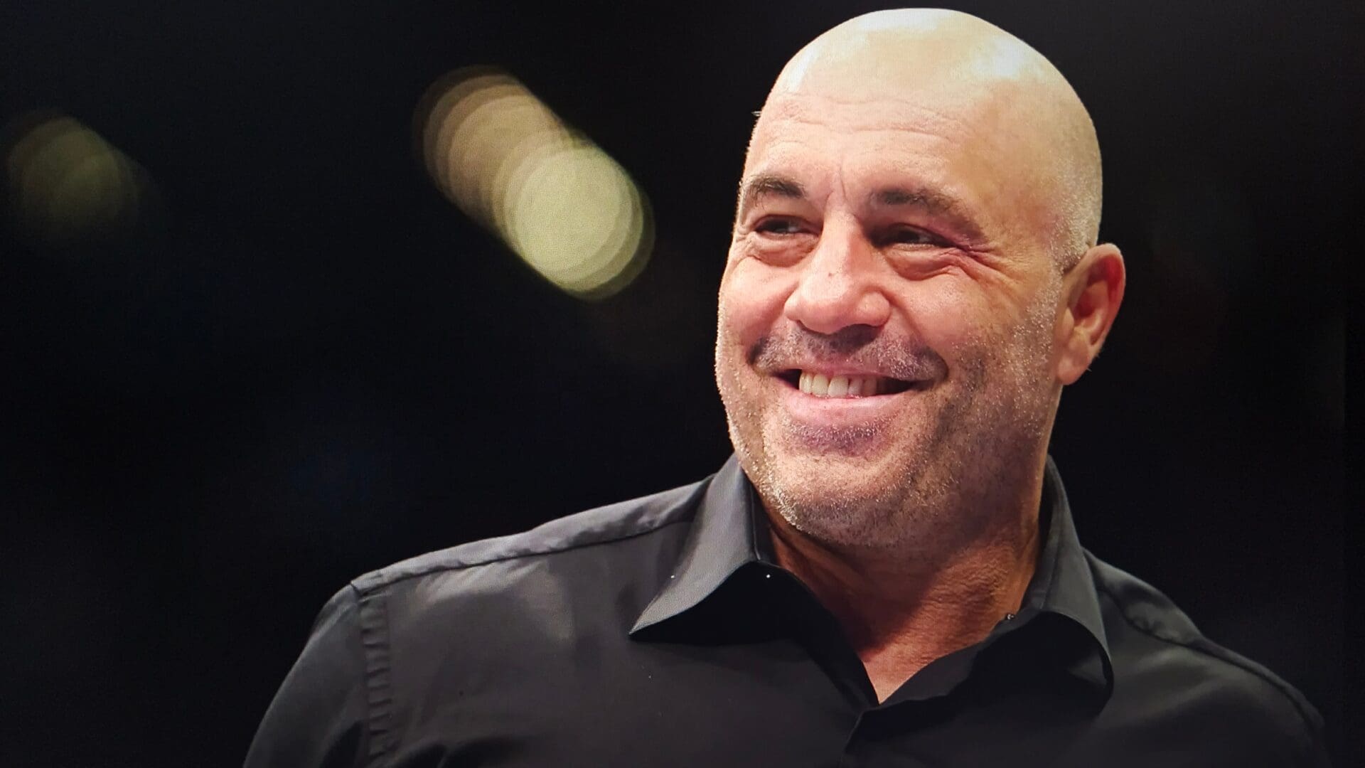 Close-up of Joe Rogan smiling against a blurred dark background