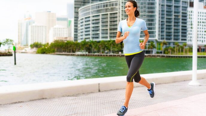 A smiling woman jogs along a waterfront path in downtown Miami with modern buildings behind her