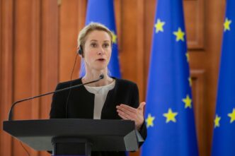 Kaja Kallas, wearing a black blazer, speaks at a press conference with European Union flags behind her