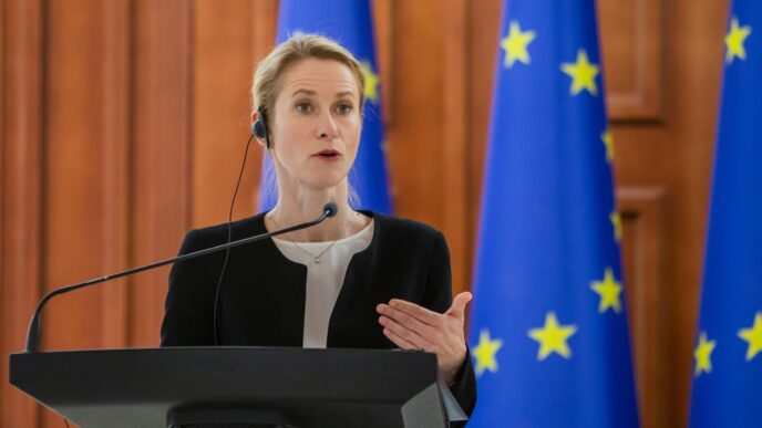 Kaja Kallas, wearing a black blazer, speaks at a press conference with European Union flags behind her