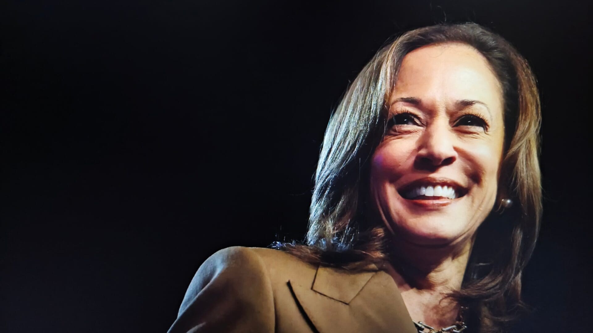 Kamala Harris smiles confidently in a portrait, wearing a brown suit jacket