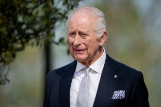 A portrait of King Charles III of the United Kingdom smiling faintly outdoors