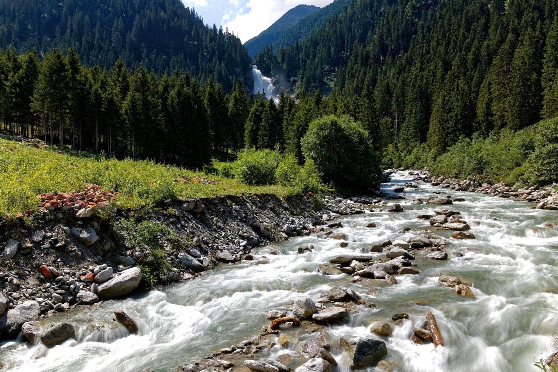 Krimml Waterfalls in Austria with a fast-flowing river and forested mountains
