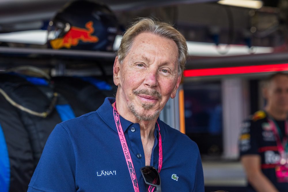A man with a goatee and blonde hair smiles at the camera with a helmet in the background