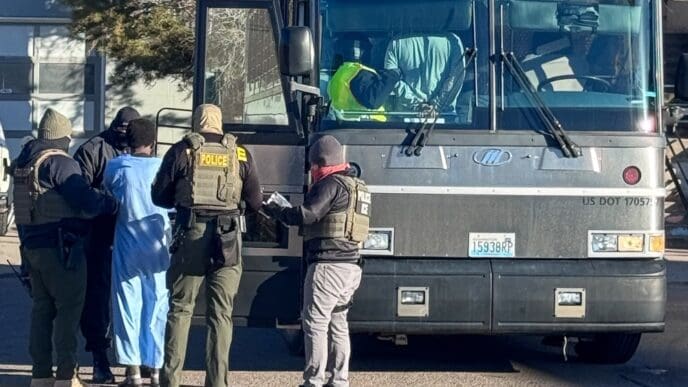Armed agents from ICE, DEA, and FBI conduct a raid, detaining a person near a large bus in Denver, Colorado