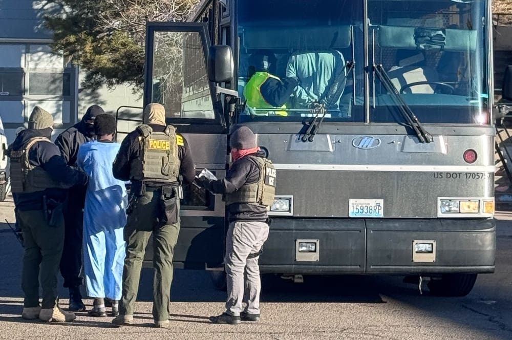 Armed agents from ICE, DEA, and FBI conduct a raid, detaining a person near a large bus in Denver, Colorado
