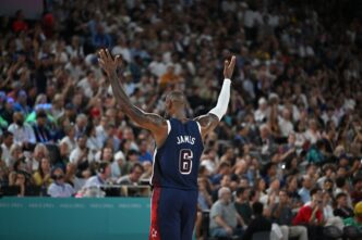 Basketball player LeBron James with his arms raised, facing a cheering crowd at an Olympic game