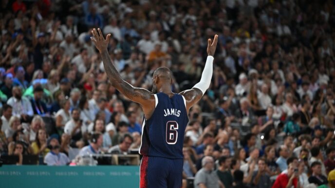 Basketball player LeBron James with his arms raised, facing a cheering crowd at an Olympic game