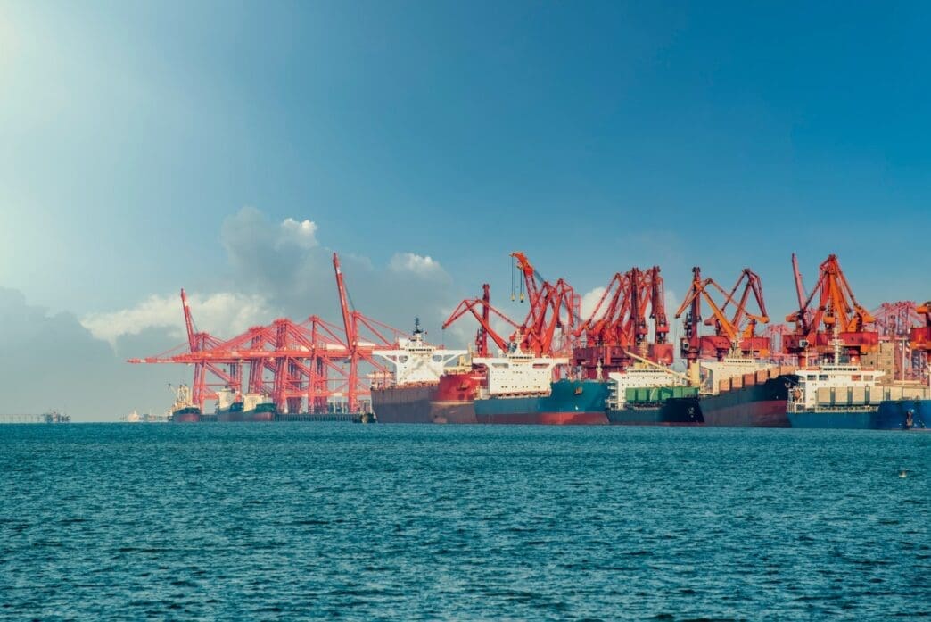 A line of large cargo ships is docked at the Lianyungang container terminal with many tall red cranes