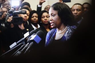 Lisa Cook, a woman with a pearl necklace, speaks into a cluster of microphones