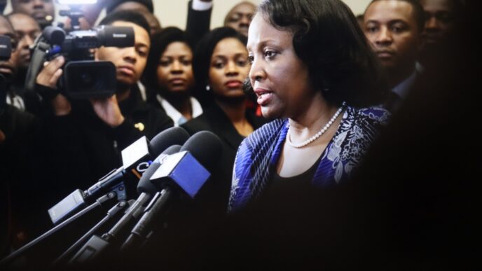 Lisa Cook, a woman with a pearl necklace, speaks into a cluster of microphones