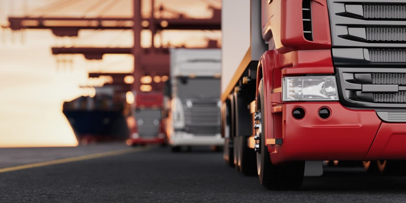 Red semi-truck in foreground with a fleet of trucks and cargo ship at a logistics hub