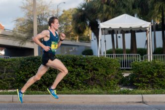 A male runner in a blue singlet and black shorts is running a race on a street