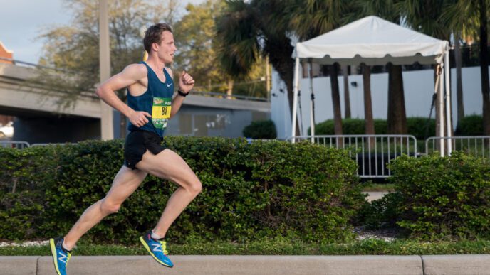 A male runner in a blue singlet and black shorts is running a race on a street