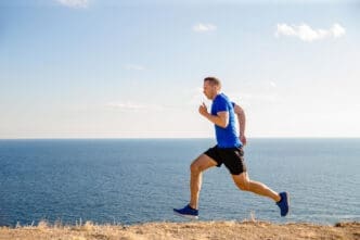 A man in athletic wear runs along a coastal path with the ocean in the background