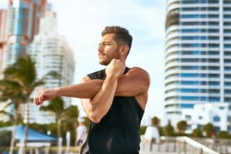 Man stretching arms outdoors with city buildings in the background