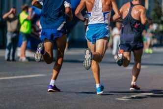 Three male runners are shown from behind, jogging on a street during a marathon
