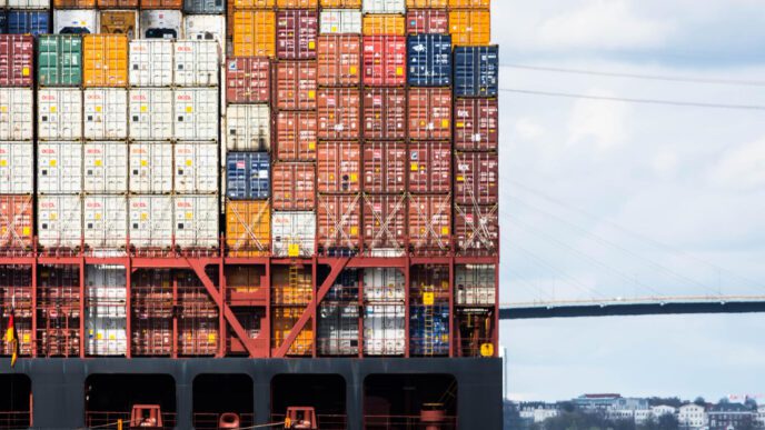The side of a large container ship is filled with stacked cargo containers in a variety of colors