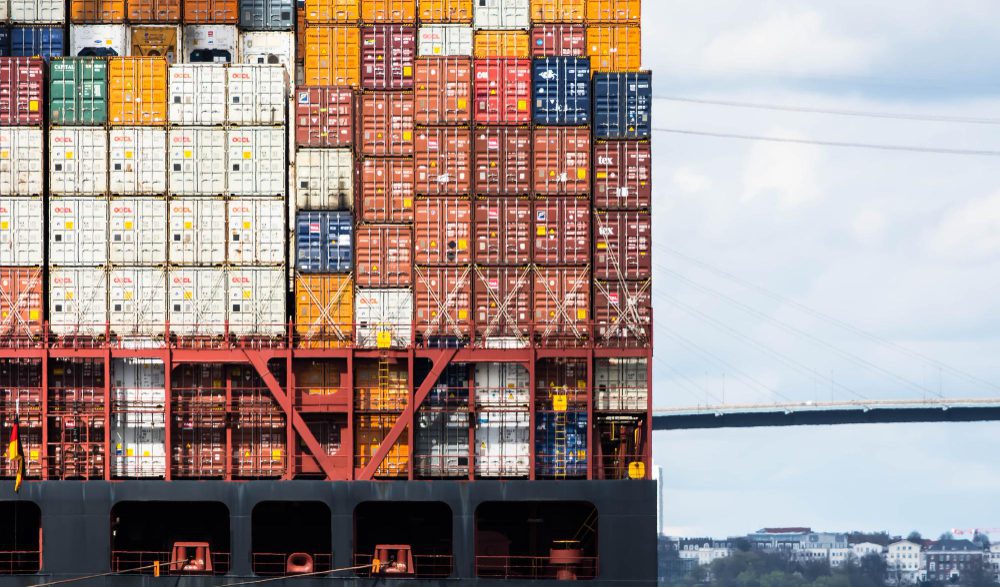The side of a large container ship is filled with stacked cargo containers in a variety of colors