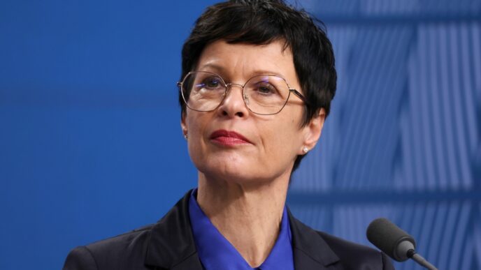 European Commissioner Marta Kos speaking at a press conference with a serious expression