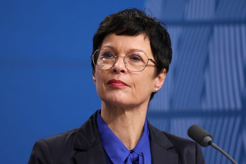 European Commissioner Marta Kos speaking at a press conference with a serious expression