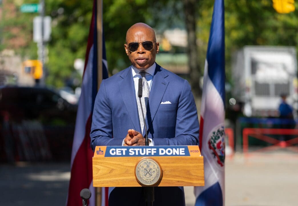 NYC Mayor Eric Adams at a podium with flags behind him during a press briefing