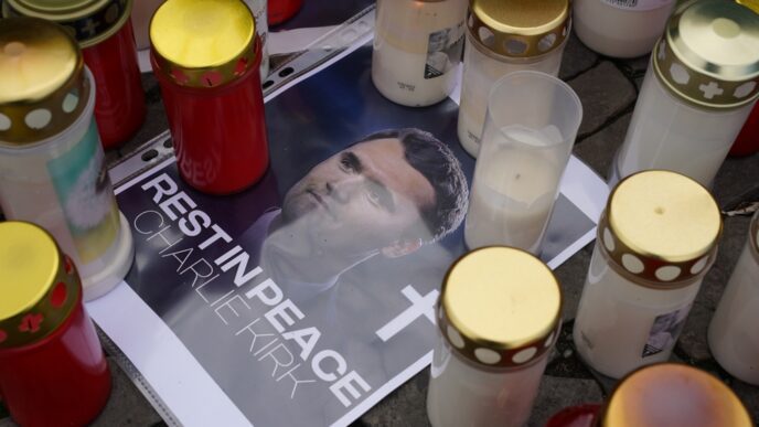 A makeshift memorial with candles and a printed photo of Charlie Kirk on a cobblestone street