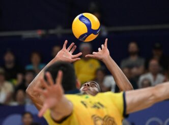 Two volleyball players jump to block a ball that is high in the air during an Olympic match