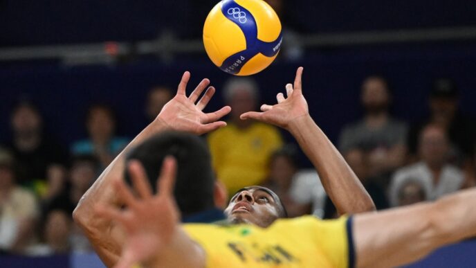 Two volleyball players jump to block a ball that is high in the air during an Olympic match