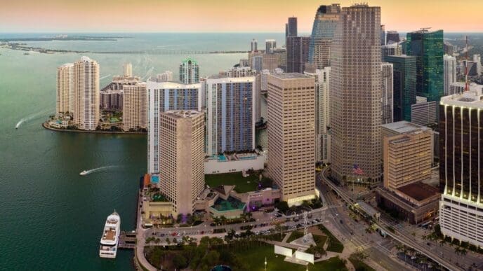 An aerial view of the downtown Miami Brickell skyline at sunset, showing modern high-rises and a waterfront with a docked ship
