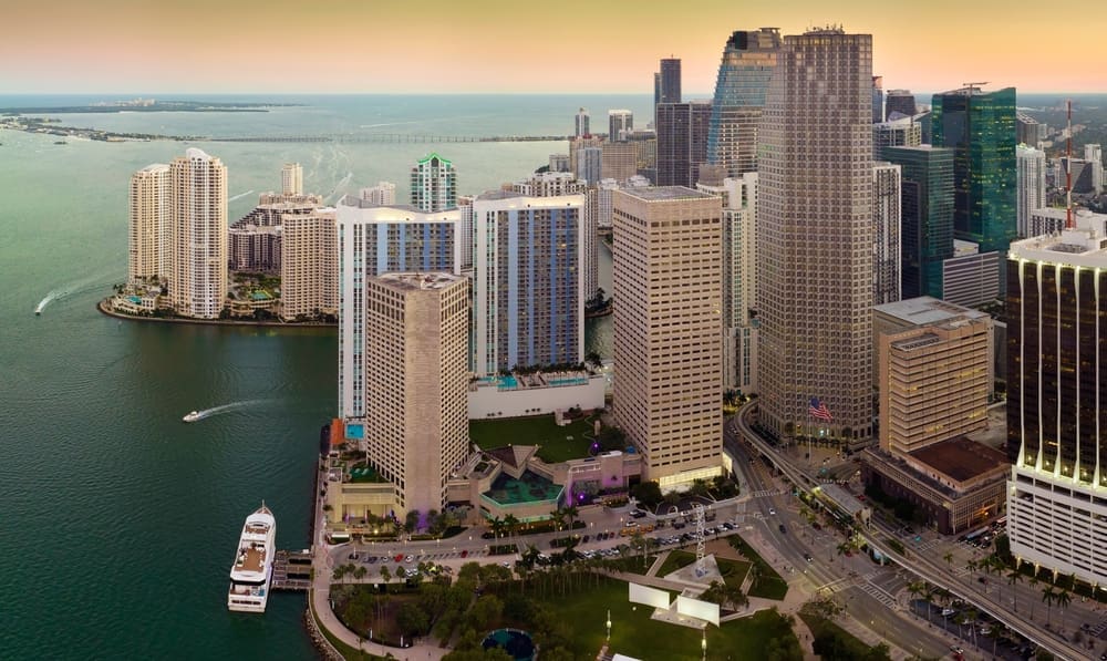 An aerial view of the downtown Miami Brickell skyline at sunset, showing modern high-rises and a waterfront with a docked ship