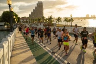 A large group of runners competes in the Miami Marathon on the Venetian Causeway at sunrise