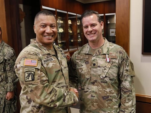 Two military officers, Harrison and Quiñones, shake hands and smile