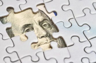 A puzzle with a missing piece that reveals a portion of a hundred-dollar bill