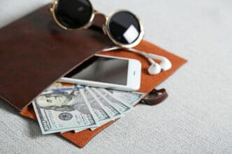 A brown leather folio holding a smartphone, earbuds, and US dollar bills