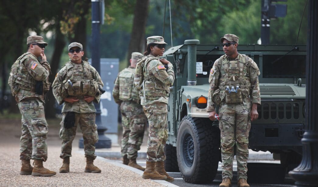 Soldiers in camouflage stand near a military vehicle on a street