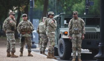 Soldiers in camouflage stand near a military vehicle on a street