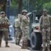 Soldiers in camouflage stand near a military vehicle on a street