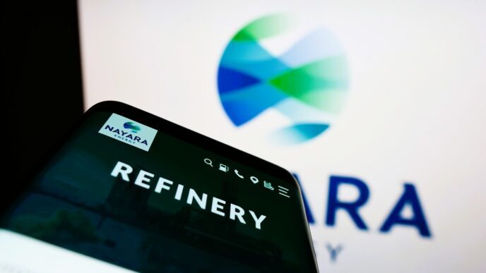A mobile phone displaying the Nayara Energy website in front of the company's logo on a screen