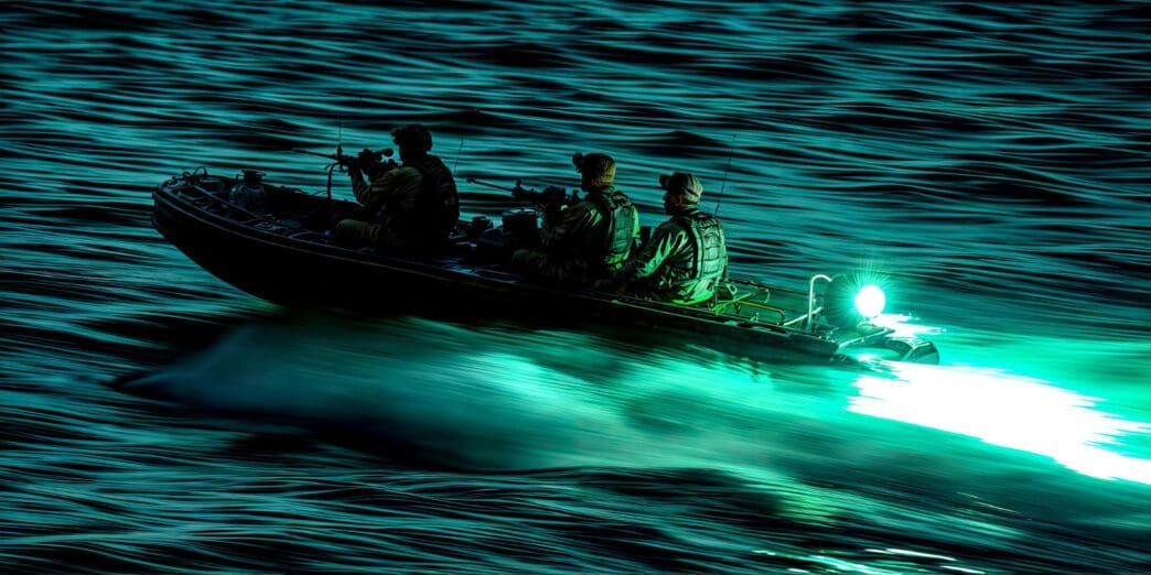 Three armed soldiers in a military-style rigid inflatable boat speed across dark, choppy water at night