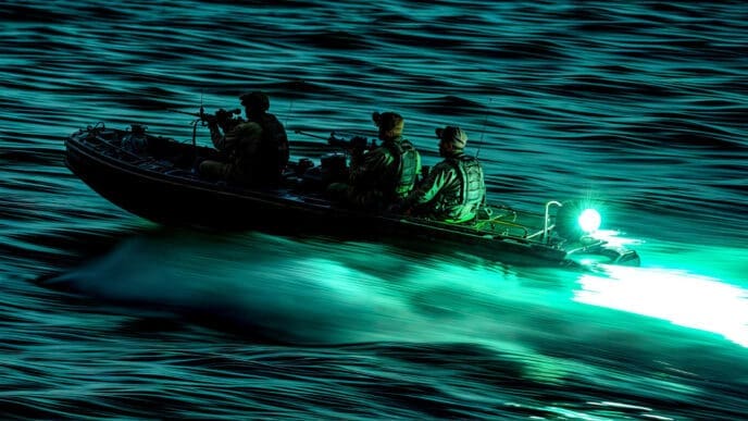 Three armed soldiers in a military-style rigid inflatable boat speed across dark, choppy water at night