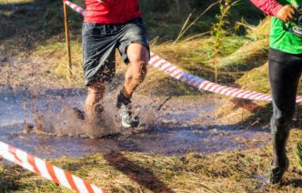 The legs of two competitors running and splashing through a muddy water obstacle during a race
