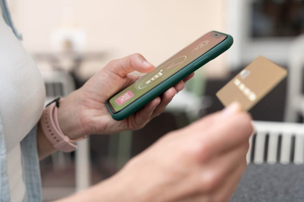 A person holds a smartphone in one hand and a gold credit card in the other, ready to make an online payment