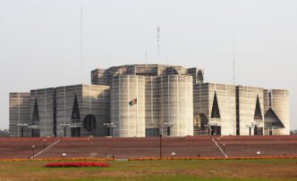 The National Parliament House of Bangladesh, a large, modern concrete building with a flag